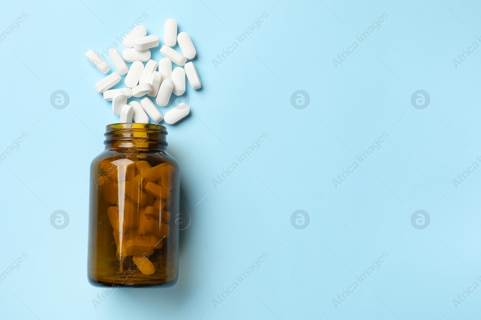 Photo of Vitamin pills and bottle on light blue background, top view. Space for text