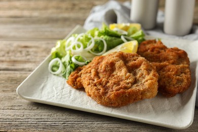 Tasty schnitzels served with lemon and salad on wooden table, closeup