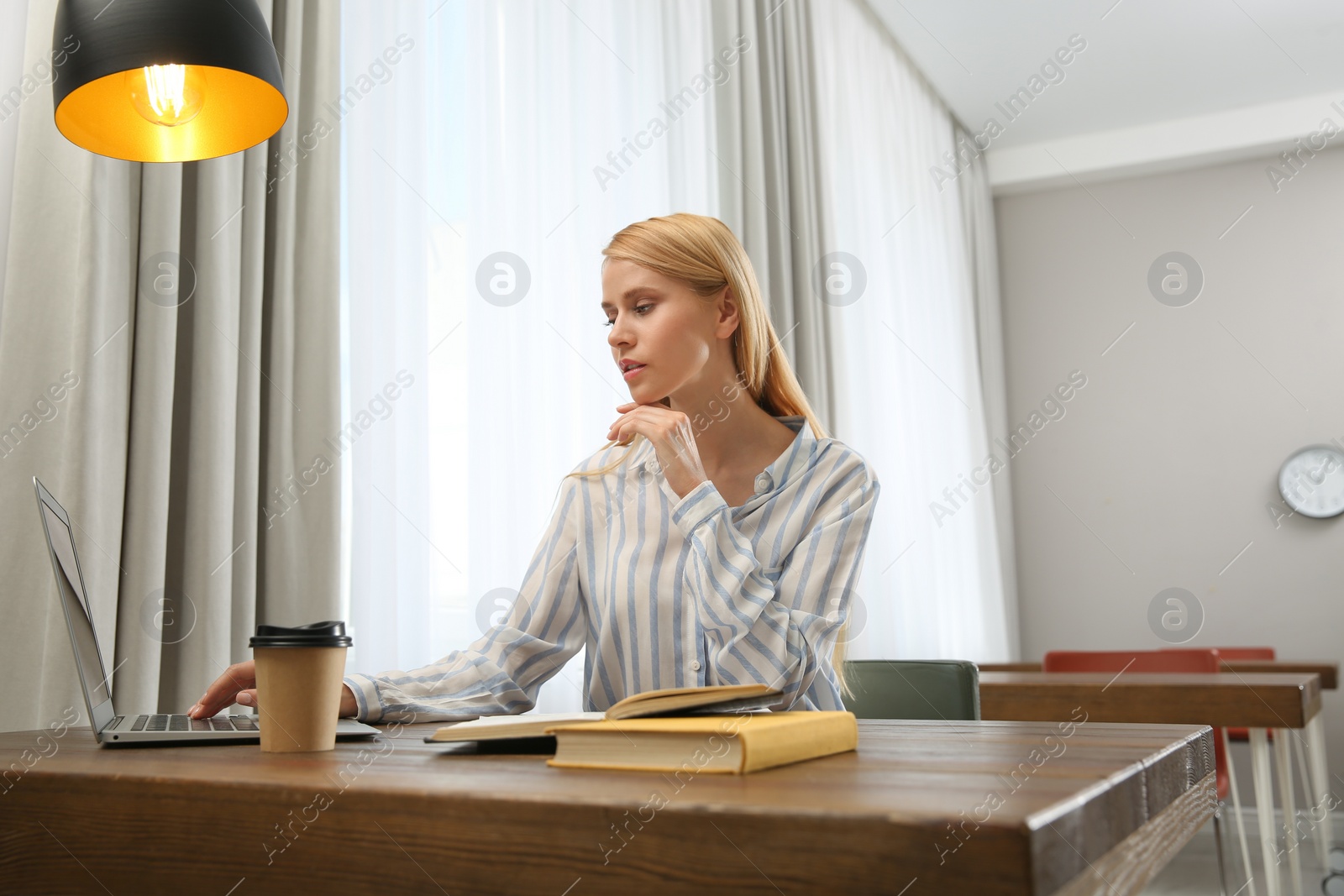 Photo of Young woman with laptop studying at table in library