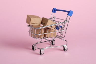 Photo of Small metal shopping cart with cardboard boxes on pink background
