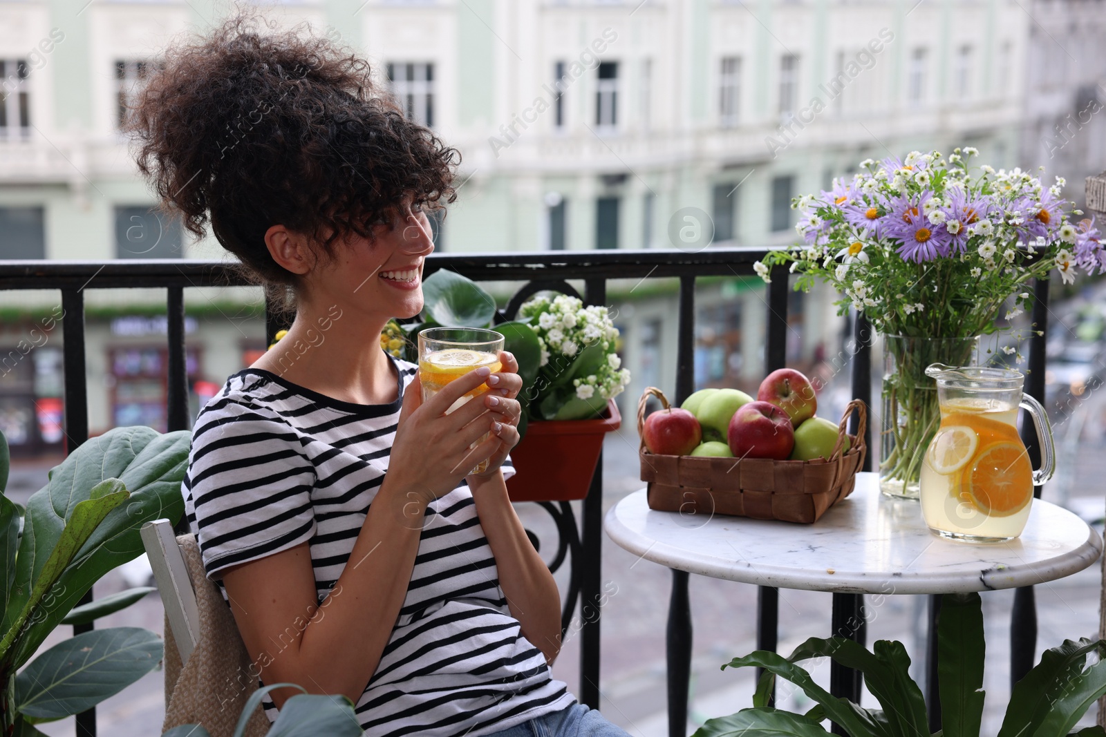 Photo of Young woman with glass of refreshing drink near beautiful houseplants on balcony