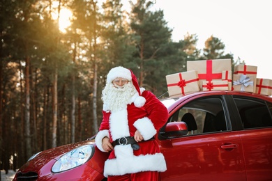 Photo of Authentic Santa Claus near red car with gift boxes, outdoors