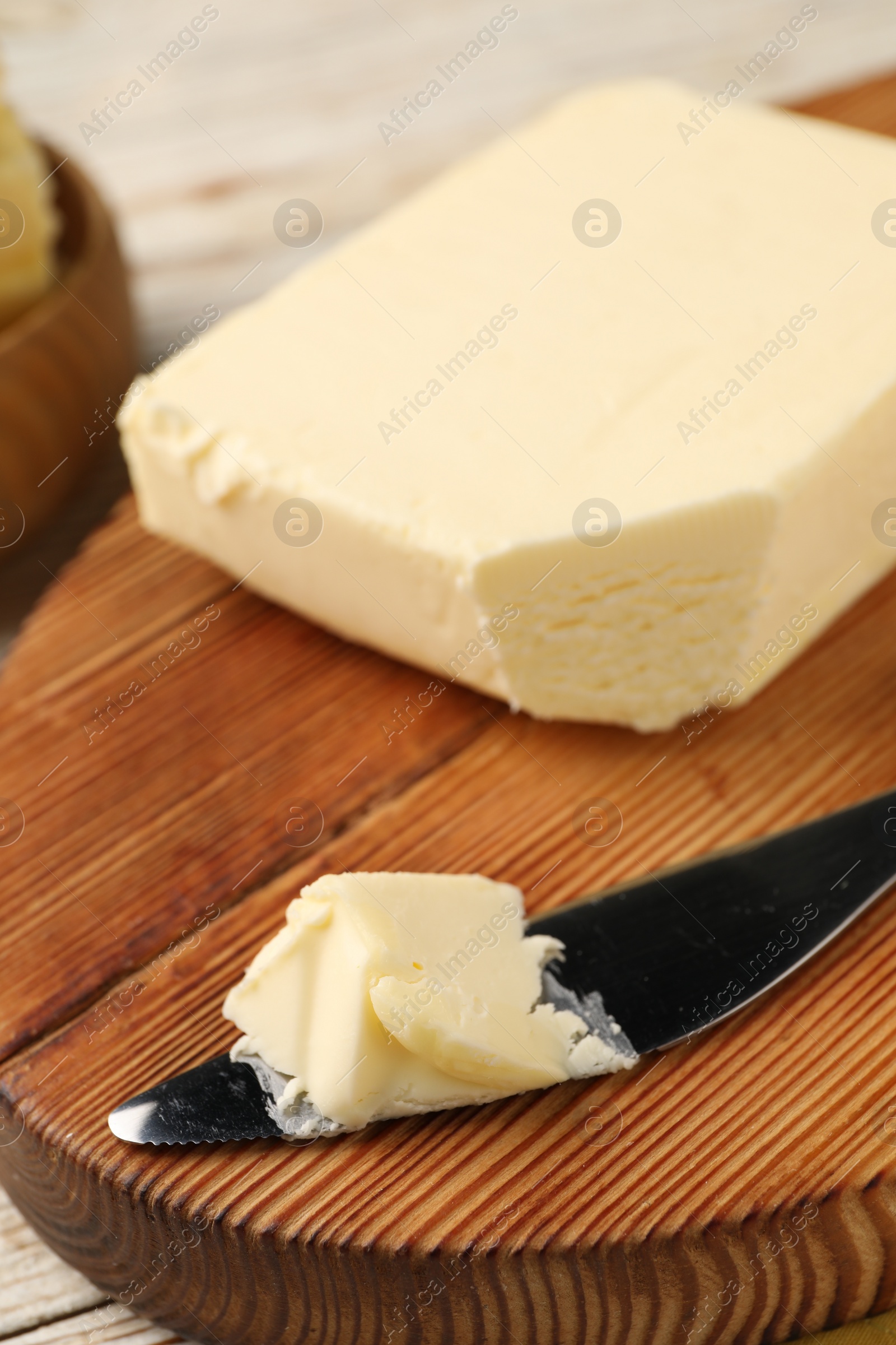 Photo of Tasty butter and knife on light wooden table, closeup