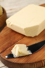 Tasty butter and knife on light wooden table, closeup