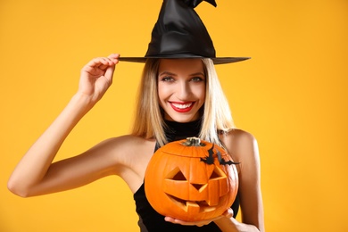 Photo of Beautiful woman in witch costume with jack o'lantern on yellow background. Halloween party