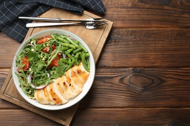 Photo of Healthy meal. Tasty salad and chicken breast in bowl and cutlery on wooden table, top view. Space for text