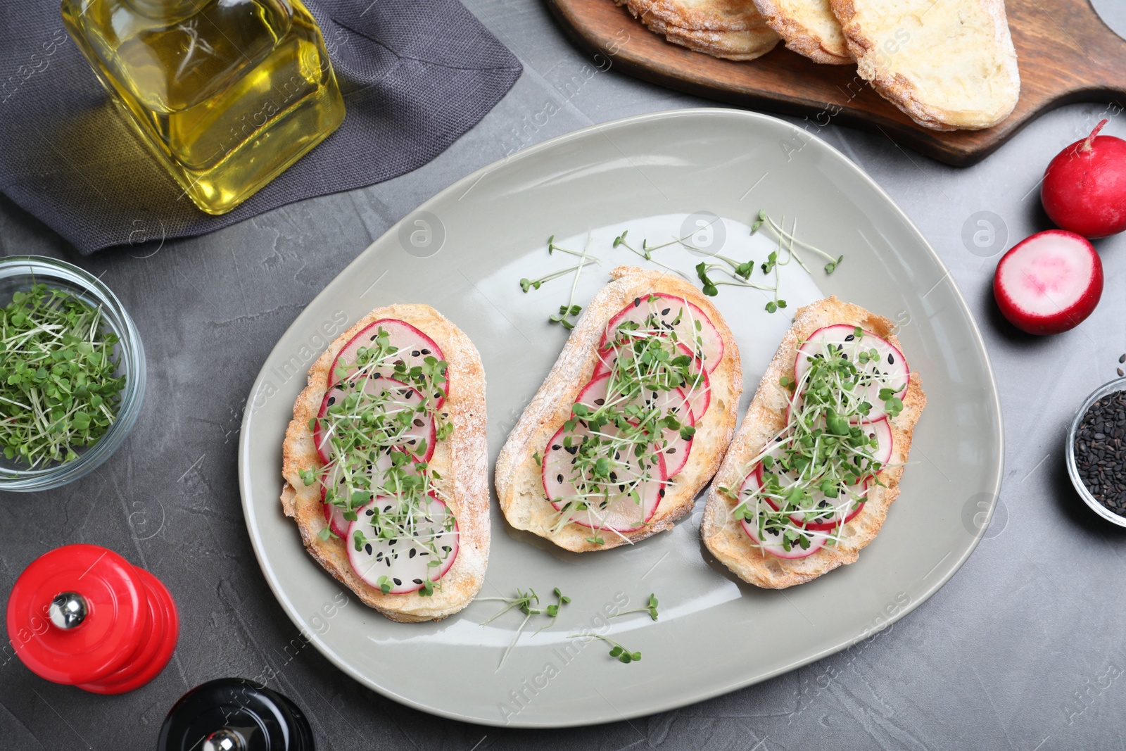 Photo of Delicious sandwiches with radish, cheese and microgreens on grey table, flat lay