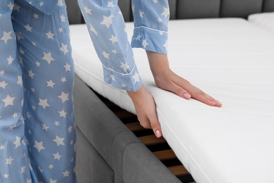 Photo of Woman putting new soft mattress on bed, closeup
