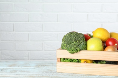 Photo of Wooden crate with fruits and vegetables on table near white brick wall, space for text