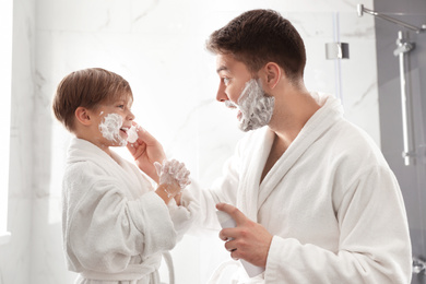 Dad applying shaving foam onto son's face in bathroom