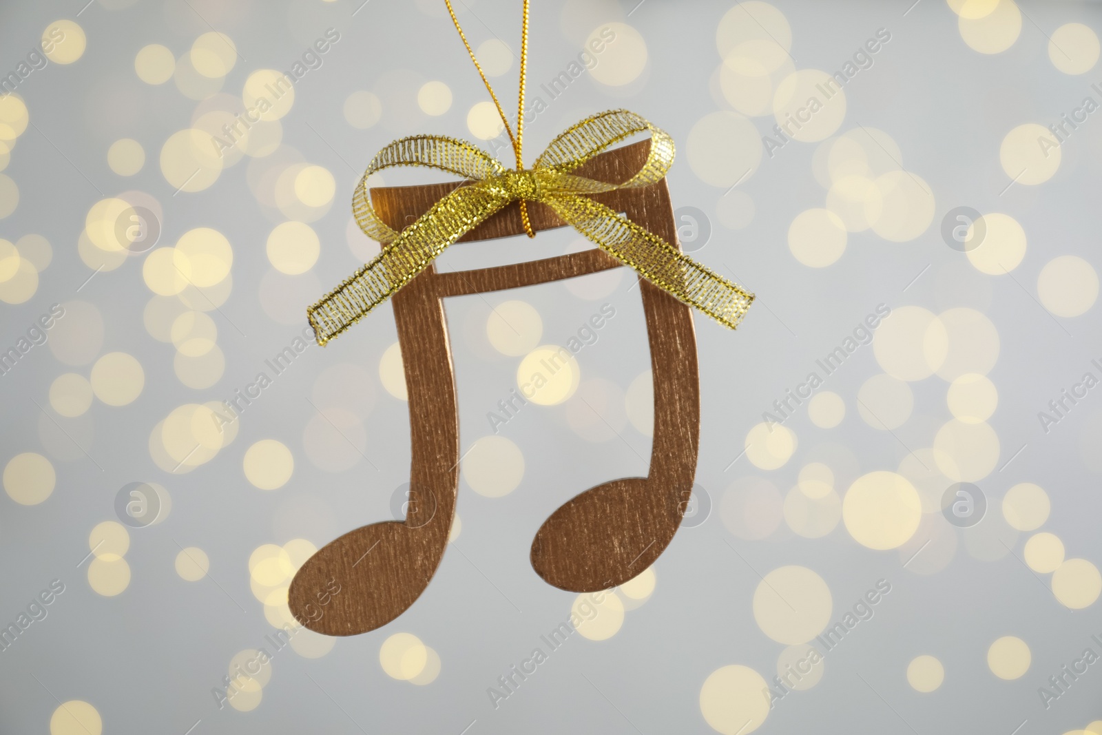 Photo of Wooden music note with golden bow hanging on light grey background with blurred Christmas lights