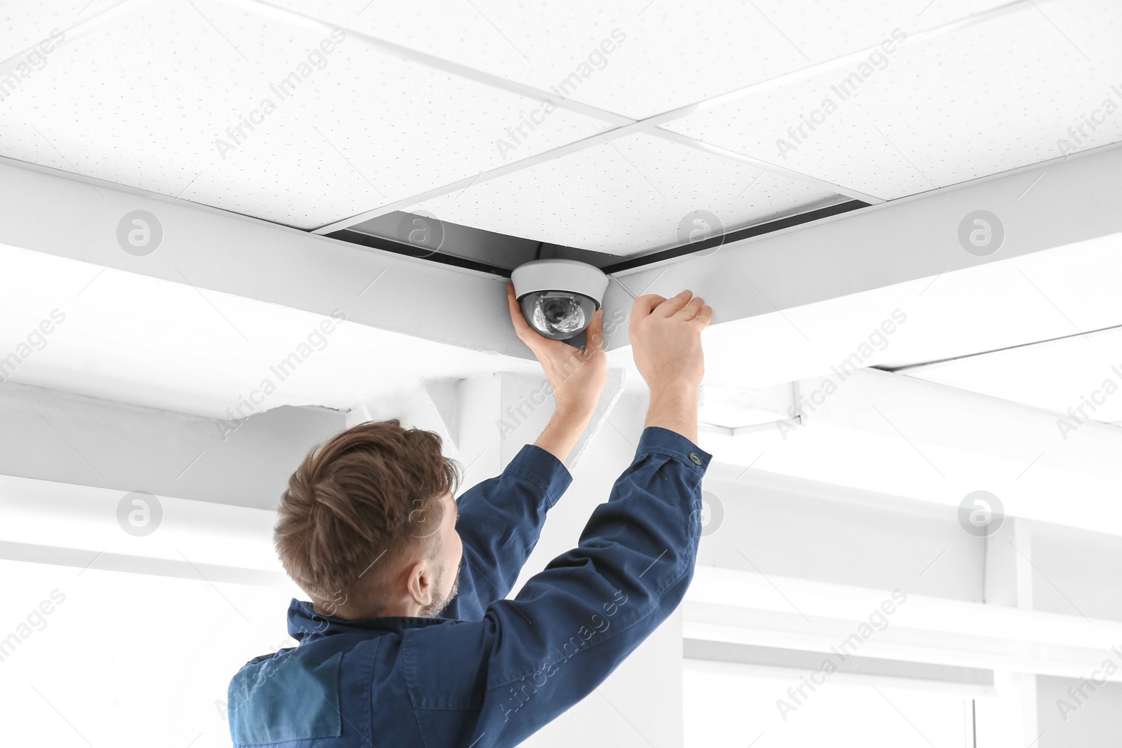 Photo of Technician installing CCTV camera on ceiling indoors