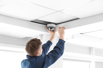 Technician installing CCTV camera on ceiling indoors