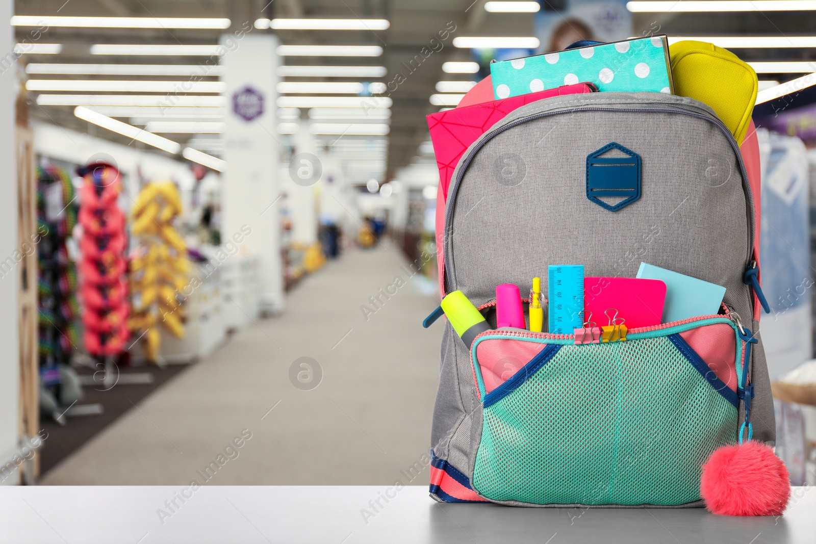 Image of Bright backpack with school stationery on table in shopping mall. Space for text