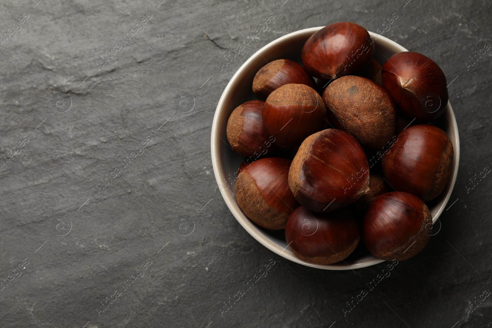 Photo of Roasted edible sweet chestnuts in bowl on grey textured table, top view. Space for text