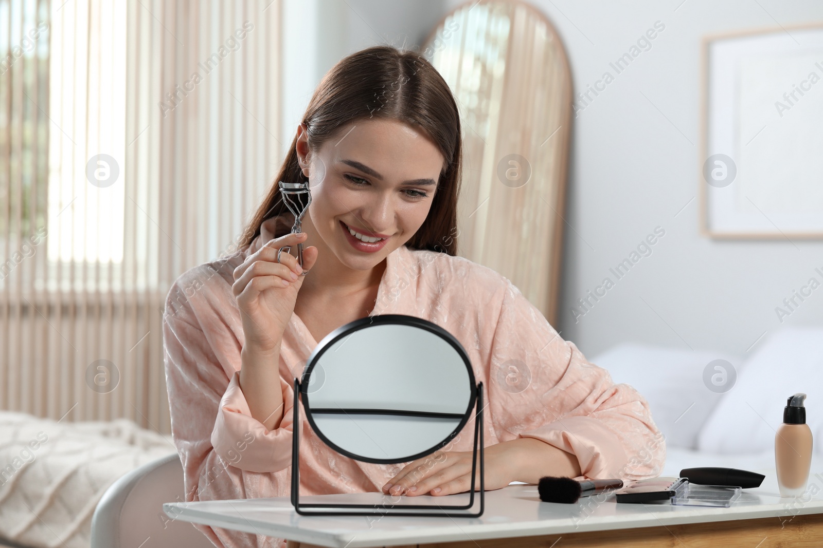 Photo of Woman with eyelash curler near mirror at home