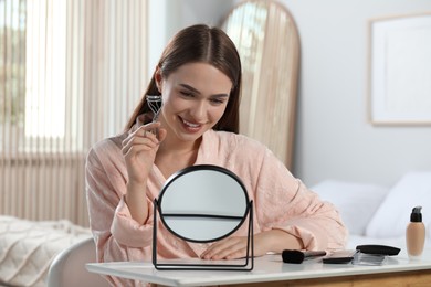 Woman with eyelash curler near mirror at home