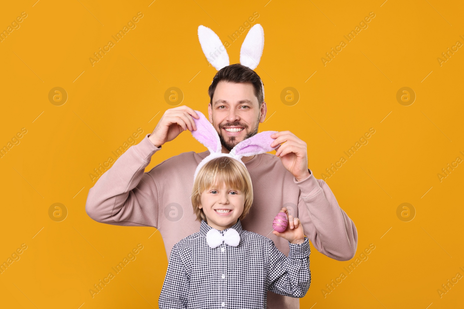 Photo of Father and son in bunny ears headbands having fun on orange background. Easter celebration