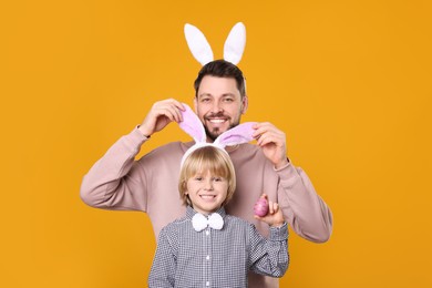 Photo of Father and son in bunny ears headbands having fun on orange background. Easter celebration