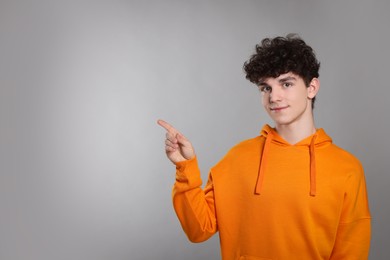 Cute teenage boy pointing at something on light grey background. Space for text