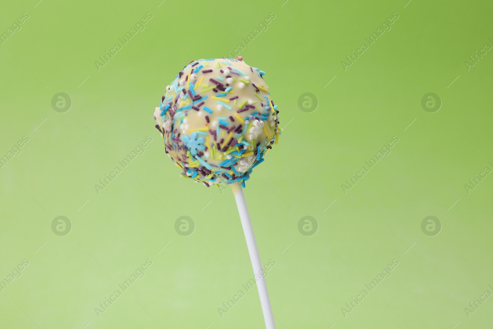 Photo of Delicious confectionery. Sweet cake pop decorated with sprinkles on light green background, closeup. Space for text