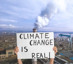 Image of Protestor holding placard with text Climate Change Is Real and blurred view of industrial factory on background 