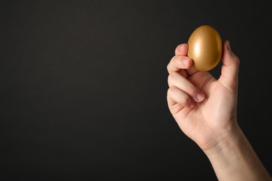 Woman holding shiny golden egg on black background, closeup. Space for text