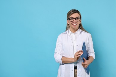 Portrait of happy doctor with clipboard on light blue background, space for text