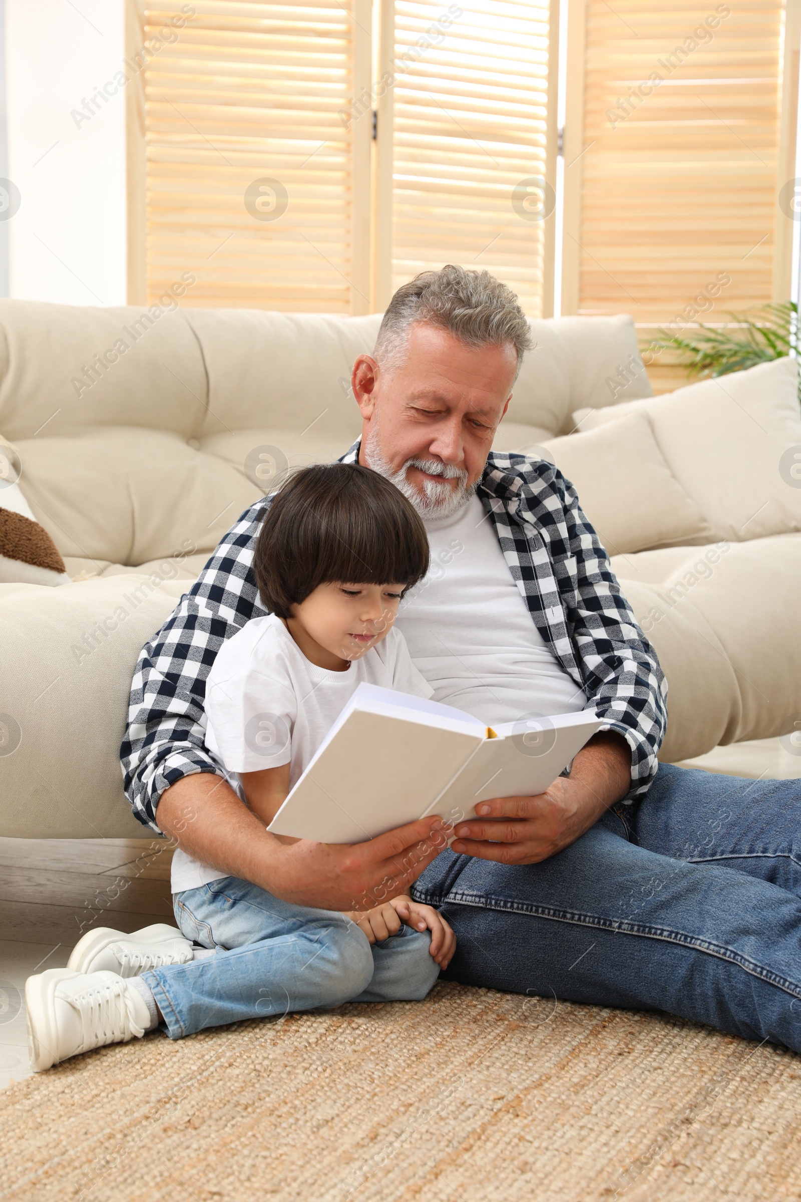 Photo of Happy grandfather with his grandson reading book together at home