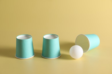 Photo of Shell game. Three paper cups and ball on yellow background