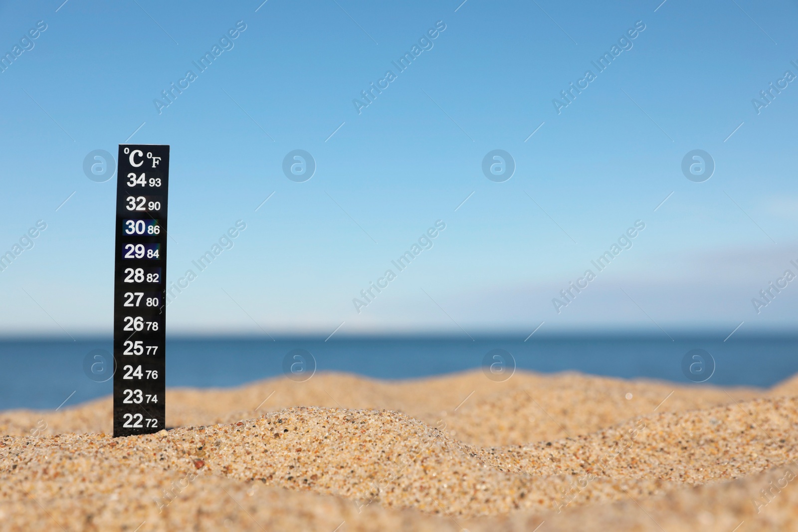 Photo of Weather thermometer in sand near sea, space for text