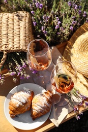 Plate with croissants and glasses of wine on wooden tray in lavender field