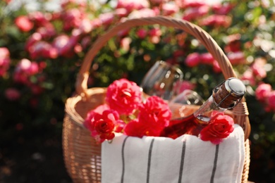 Photo of Wicker basket with bottle of wine and roses outdoors