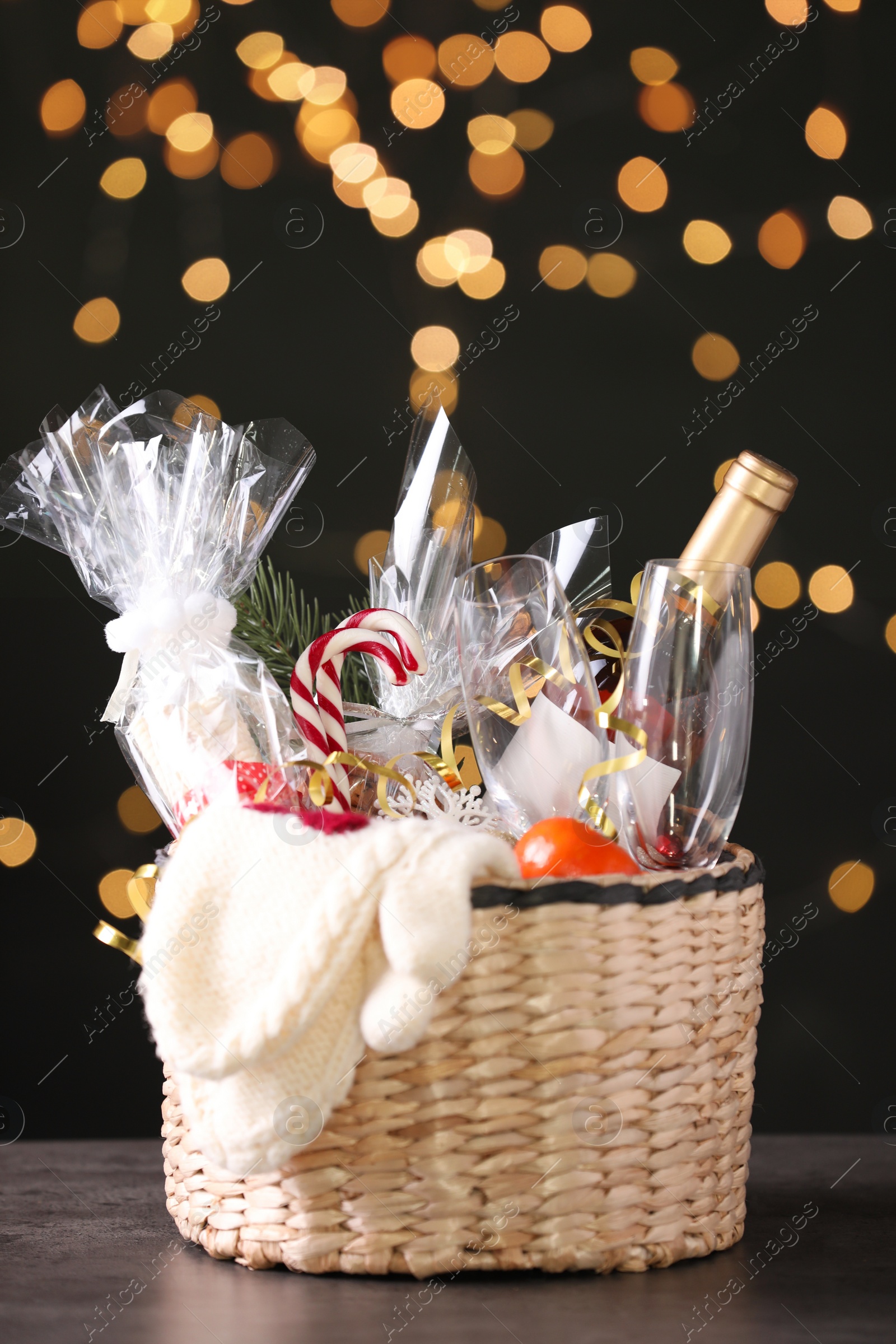 Photo of Wicker basket with Christmas gift set on grey table against festive lights