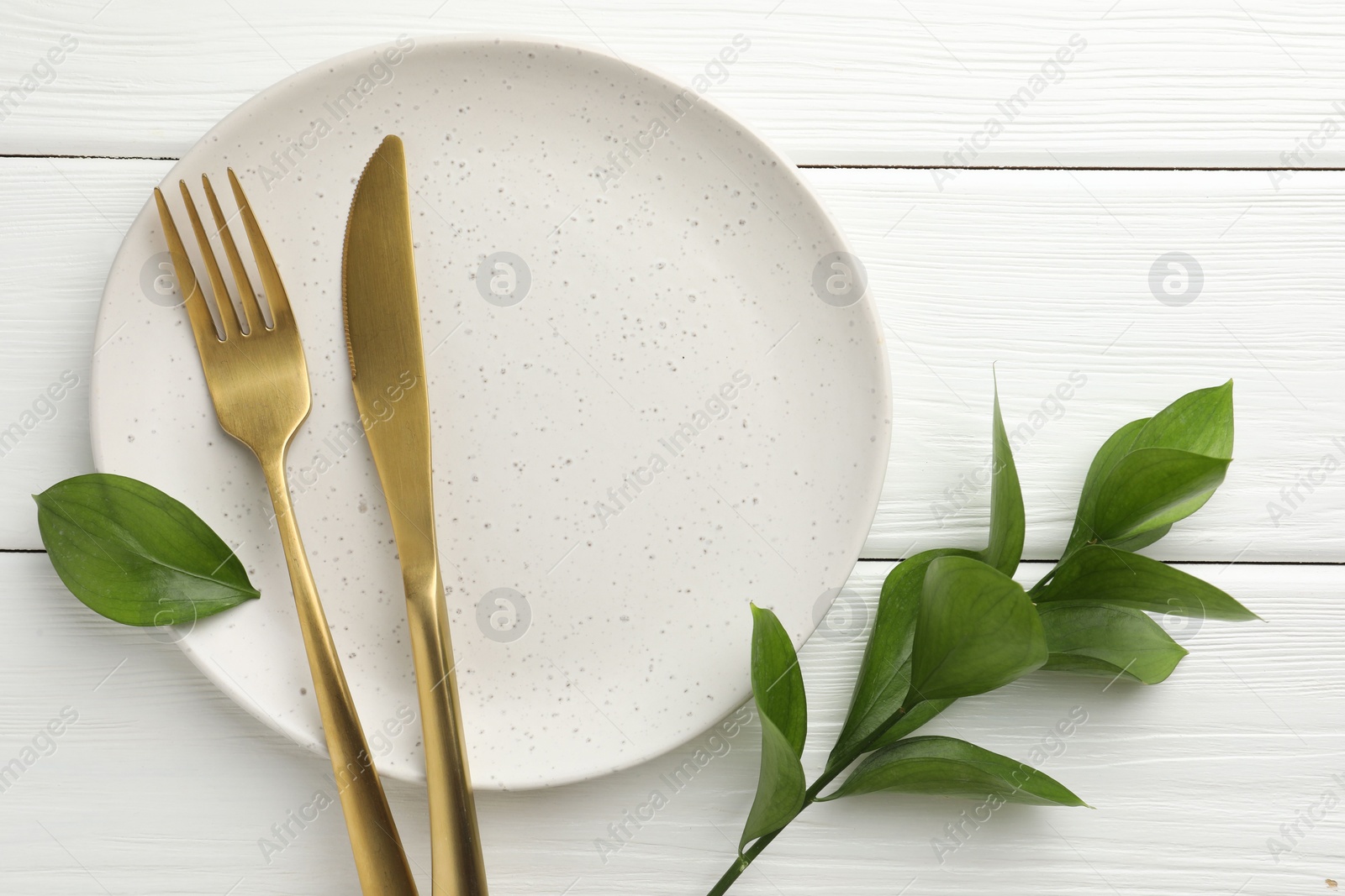 Photo of Stylish setting with cutlery, green leaves and plate on white wooden table, flat lay