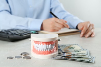 Educational dental typodont model and money on light grey table. Expensive treatment