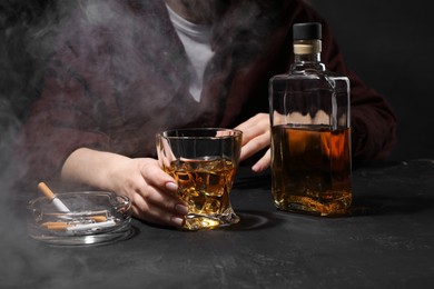 Alcohol addiction. Woman with whiskey and smoldering cigarettes at dark textured table, closeup