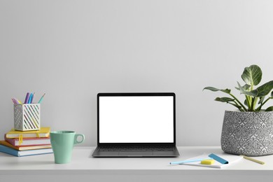 Photo of Stylish workplace with laptop, houseplant, stationary and cup on table near white wall