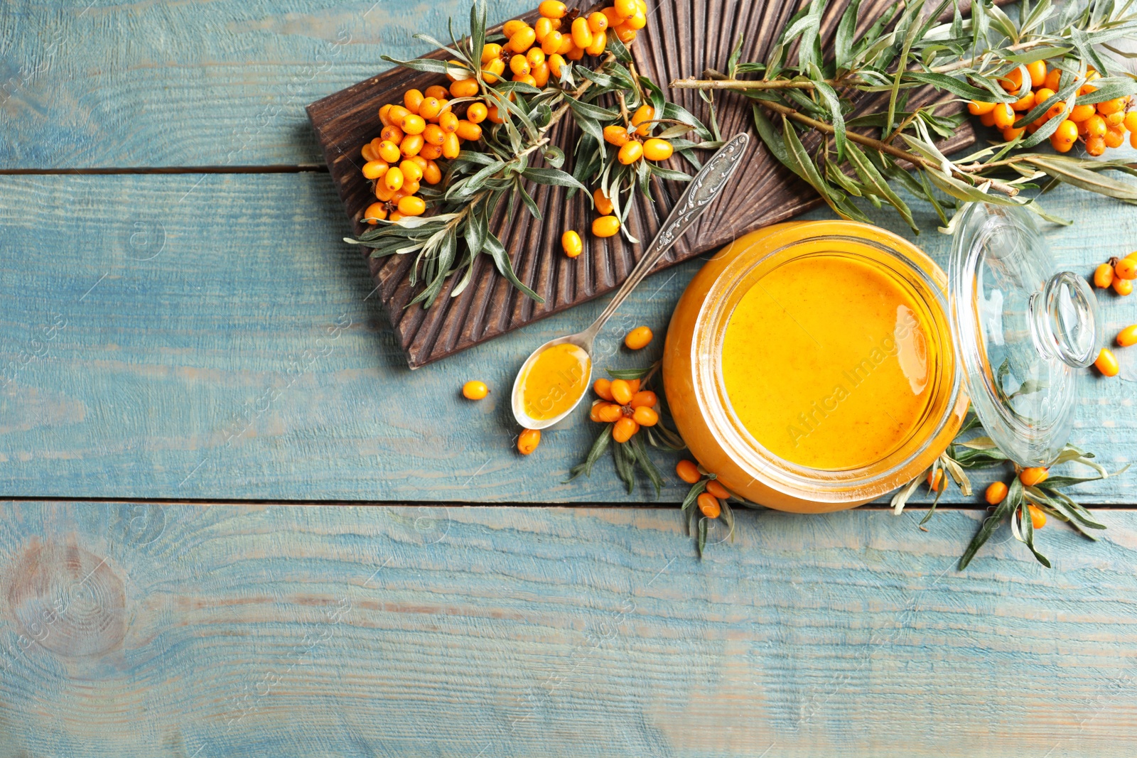 Photo of Delicious sea buckthorn jam and fresh berries on blue wooden table, flat lay. Space for text