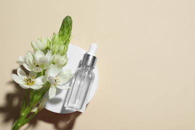 Bottle of cosmetic oil and flowers on beige background, top view. Space for text