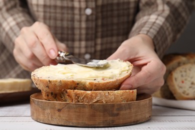 Photo of Woman spreading butter onto bread at white wooden table, closeup