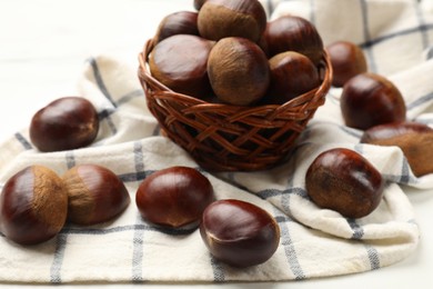 Photo of Sweet fresh edible chestnuts in wicker bowl on white table, closeup