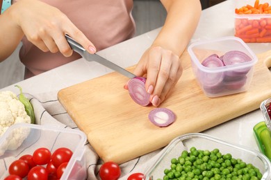 Photo of Woman cutting onion and containers with fresh products on light gray table, closeup. Food storage