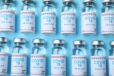 Photo of Glass vials with COVID-19 vaccine on light blue background, flat lay