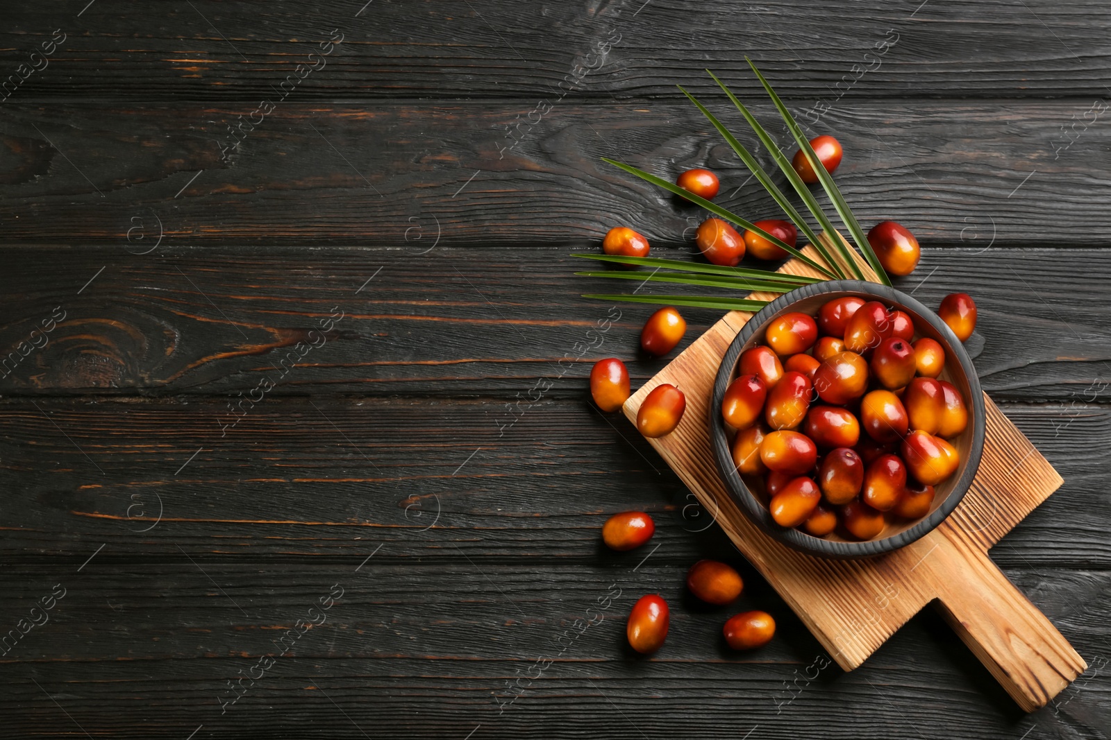 Image of Palm oil fruits in bowl on black wooden table, flat lay. Space for text