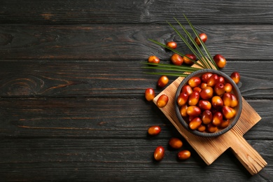 Image of Palm oil fruits in bowl on black wooden table, flat lay. Space for text