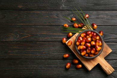 Palm oil fruits in bowl on black wooden table, flat lay. Space for text