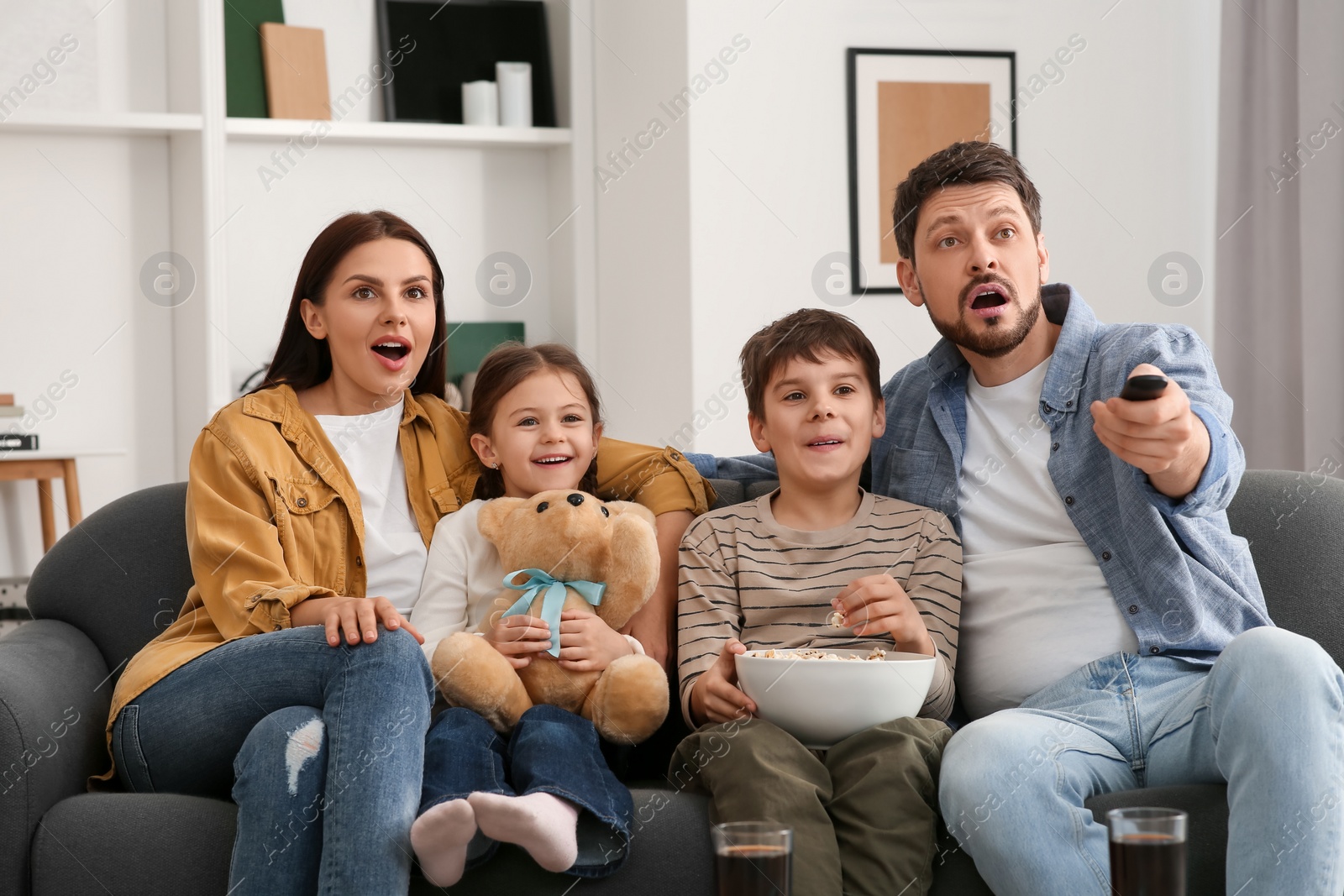 Photo of Emotional family watching TV at home. Father changing channels with remote control