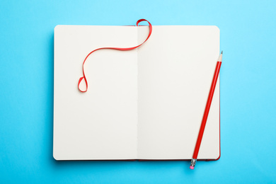 Stylish open notebook and pencil on light blue background, top view