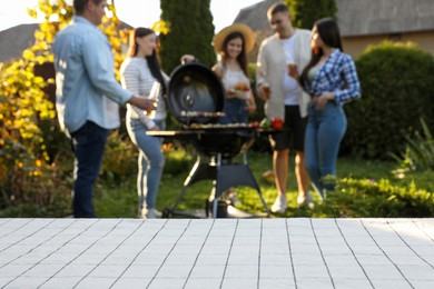 Empty white wooden table and blurred view of friends having barbecue party outdoors. Space for text